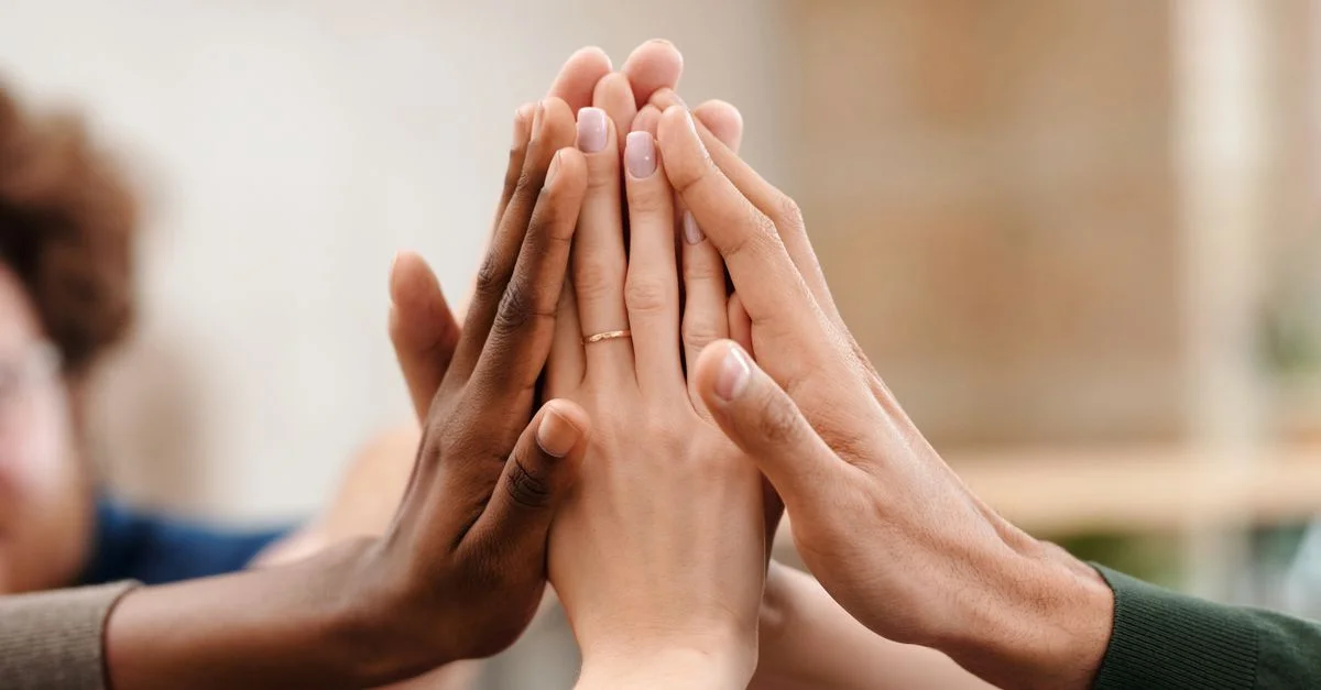 Nahaufnahme von Händen einer diversen Gruppe, die sich abklatschen und Teamarbeit sowie Einheit symbolisieren.
