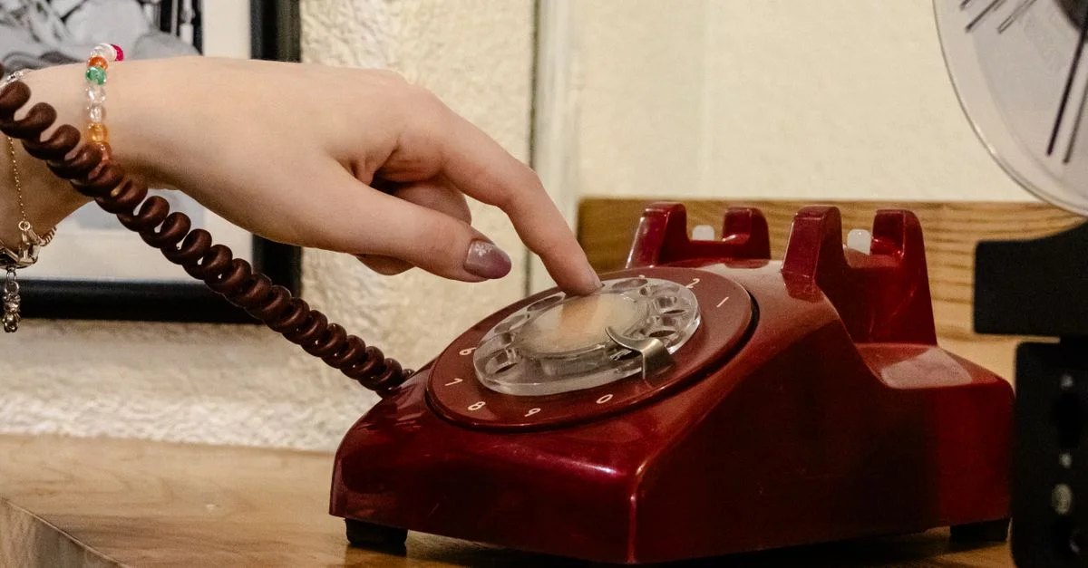Eine Nahaufnahme einer Hand, die ein klassisches rotes Wählscheiben-Telefon wählt und Nostalgie einfängt.