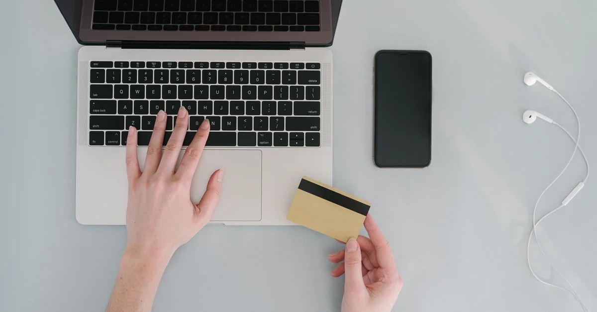 Vogelperspektive auf einen Arbeitsplatz mit einem Laptop, Bankkarte, Smartphone und Kopfhörern, ideal für Online-Finanzthemen.