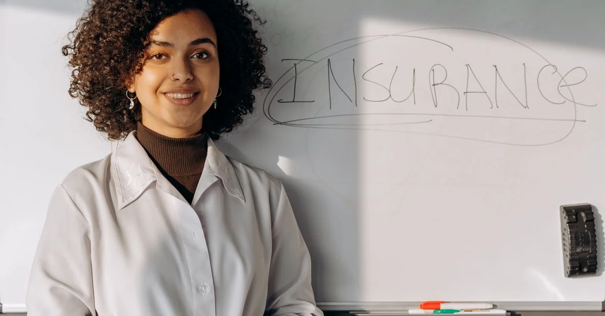Afrikanisch-amerikanische Frau lächelt in einem Büroumfeld mit einem Whiteboard, auf dem 'Versicherung' steht.