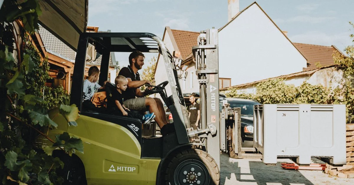 Eine Familie mit Kindern genießt an einem sonnigen Tag eine Fahrt mit einem Gabelstapler in einem Wohngebiet.