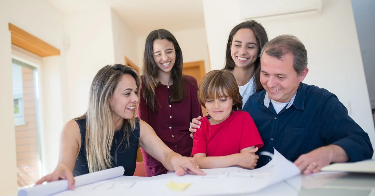 Eine fröhliche Familie versammelt sich um einen Tisch, um zusammen einen Bauplan für ein Haus zu überprüfen.