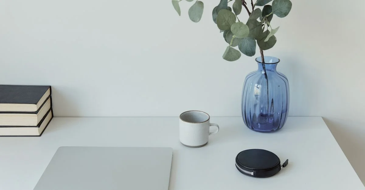 Sauberer, minimalistischer Schreibtisch mit Laptop, blauer Vase mit Pflanze und Kaffeetasse.