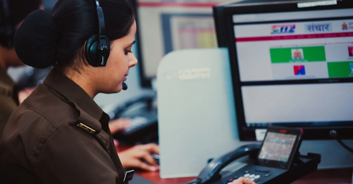 Konzentrierter Callcenter-Dispatcher in Uniform, der am Computer mit Headset in einer Büroumgebung arbeitet.