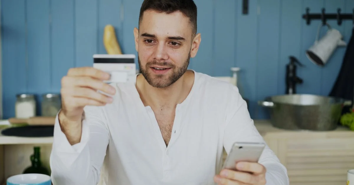 Mann hält eine Kreditkarte und ein Smartphone, kauft online zu Hause ein.