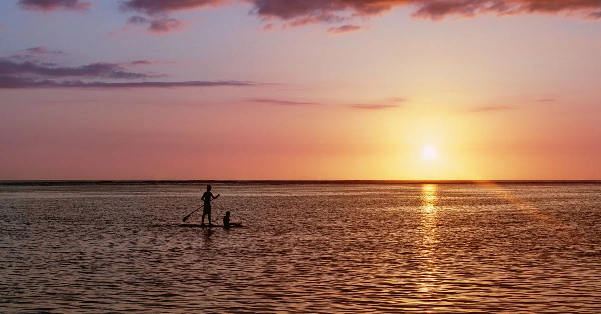 Ein lebhafter Sonnenuntergang über dem Ozean mit Silhouetten von Paddleboardern auf der Insel Réunion.