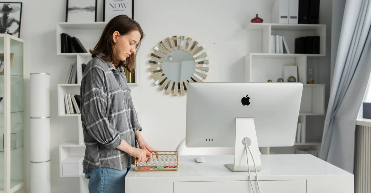 Erwachsene Frau organisiert ihren Schreibtisch mit einem Desktop in einem modernen, stilvollen Büro mit Regalen und Dekoration.