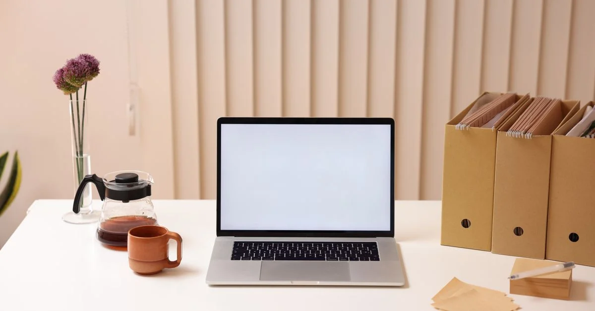 Ein minimalistischer Arbeitsbereich mit einem Laptop, Ordnerorganisatoren und Kaffee, ideal für Produktivität.