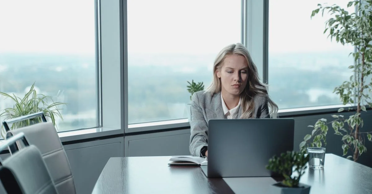 Professionelle Frau, die an einem Laptop in einem modernen Büro mit großen Fenstern arbeitet.